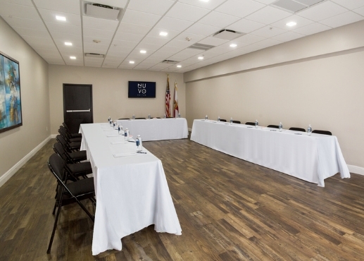 Sala de conferencias con 3 mesas largas con manteles blancos y sillas plegables negras