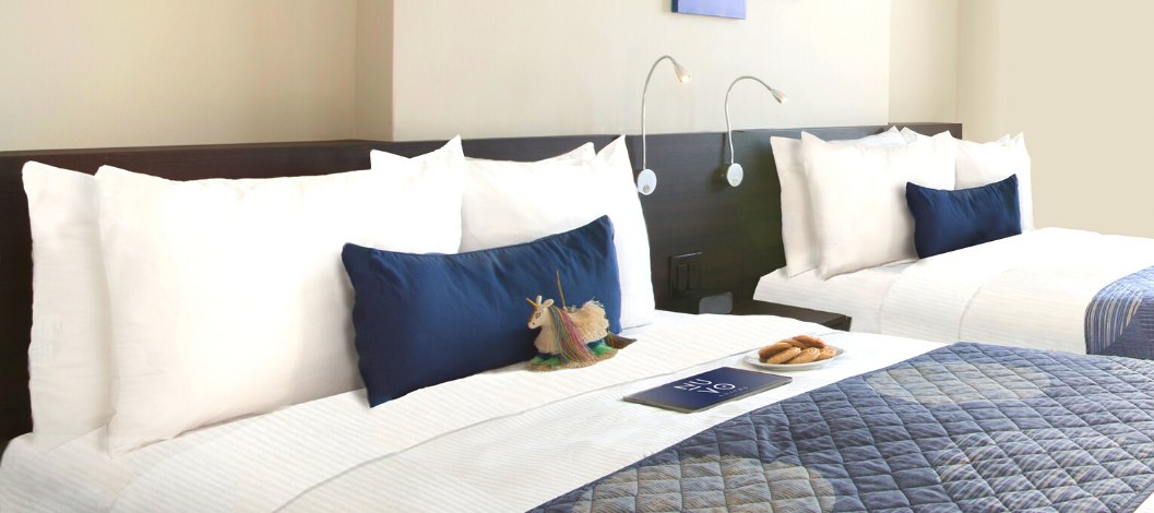 Dos camas queen con almohadas azules y blancas y sábanas con un plato de galletas