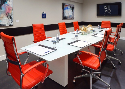 Sala de reuniones con una mesa blanca, diez sillas de color melocotón, pinturas en las paredes, y una televisión de pantalla plana