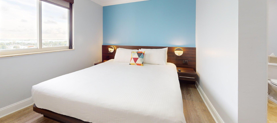 Cama King con cabecera oscura y almohadas y sábanas blancas