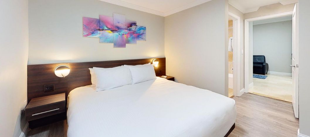 Cama King con cabecera oscura y almohadas y sábanas blancas